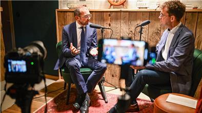 Mann mit Brill gestikuliert mit der Hand und spricht ins Mikrofon.