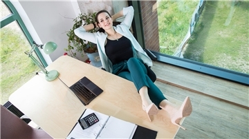 Eine Frau legt entspannt ihre Beine auf den Schreibtisch und genießt die Vier-Tage-Woche.
