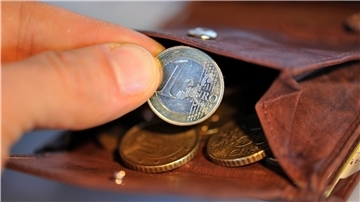Eine Hand nimmt eine Ein-Euro-Münze aus einer braunen Brieftasche und hält sie in die Kamera.