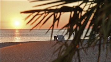 Zwei Menschen stehen neben einem Strandkorb am Strand und beobachten den Sonnenuntergang.