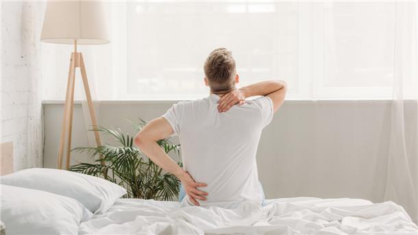 Ein Mann, der offensichtlich Rückenschmerzen hat, sitzt auf einem Bett.