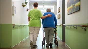 Eine Pflegekraft hilft einem Patienten, der auf den Rollator angewiesen ist, bei der Fortbewegung.