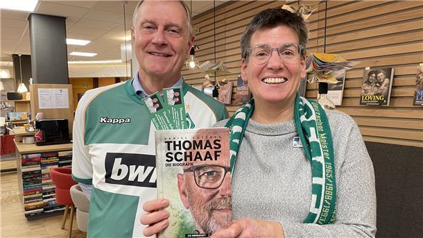 Ein Mann und eine Frau mit der Biografie von Thomas Schaaf. Werder-Fan Rolf Ahlers und Buchhändlerin Anne von Bestenbostel freuen sich auf die Lesung mit der Trainer-Legende. 