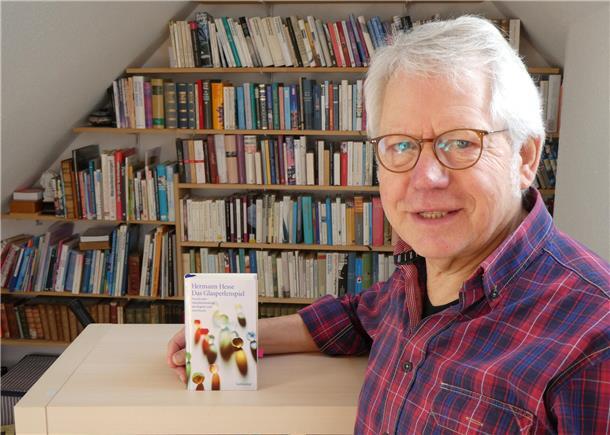 „Das Glasperlenspiel“: Die Antwort auf die Frage nach einem glücklichen Leben Ein Mann vor einem Bücherregal. Auf dem Tisch steht ein Buch. Das Foto zeigt Werner Stelljes.
