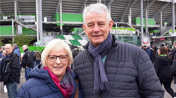 Ein älteres Ehepaar in blauen Daunenjacken steht vor einem Fußballstadion.