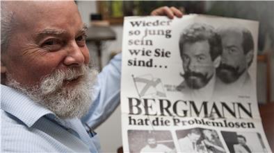 Wilhelm Schaawé hält ein Plakat aus früheren Zeiten hoch. Es zeigt ihn als Toupetmodel.