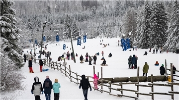 Wintersportler gehen mit ihren Schlitten an einem Rodellift im Harz entlang.
