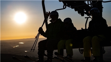 Wintersportler sitzen bei Sonnenaufgang im Sessellift.