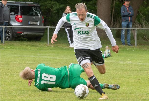 Ein Mann mit einem Ball am Fuß läuft an einem am Boden liegenden vorbei.