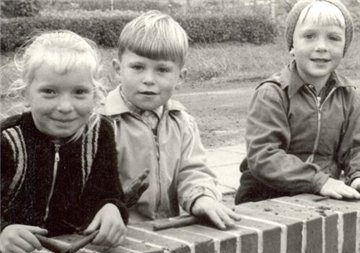 Wo haben die fröhlich über eine Mauer schauenden Kinder denn den Ton her, den sie gerade zu Würstchen ausrollen? Doch nicht etwa von der Baustelle?