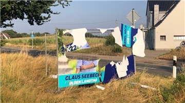 Ein abgerissenes Plakat an einem Bauzaun an einer Straße.