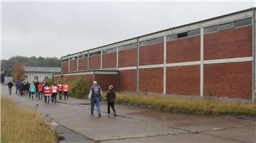 Eine Menschengruppe läuft an einer Backstein-Lagerhalle entlang.