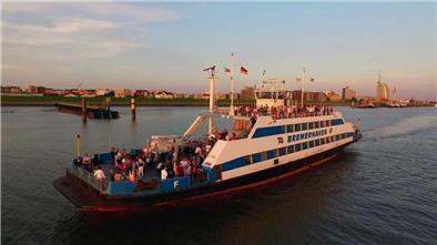 Schiff mit vielen Personen an Bord fährt bei Sonnenuntergang über die Weser, im Hintergrund Bremerhaven
