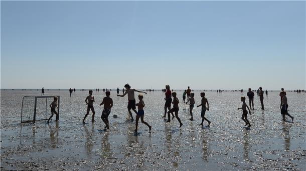 Kinder spielen im Watt Fußball. Im Ferienpass der Gemeinde Wurster Nordseeküste wird Wattfußball angeboten.