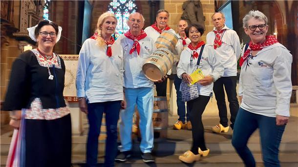 Frauen und Männer in traditioneller Kleidung mit zwei Fässern lächeln in die Kamera.
