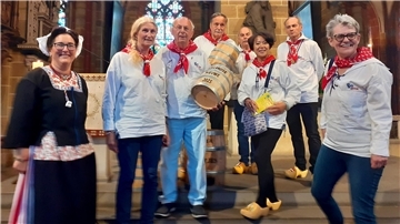 Frauen und Männer in traditioneller Kleidung mit zwei Fässern lächeln in die Kamera.