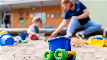 Bild einer Erzieherin, die mit einem Kind im Sandkasten spielt