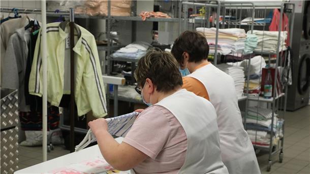Zwei Frauen arbeiten in der Wäscherei der Lebenshilfe Gera e.V und legen dort Wäsche zusammen.