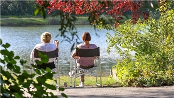Zwei Frauen sitzen im baden-württembergischen Ertingen an einem See in der Sonne.