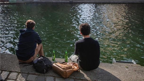 Zwei junge Männer trinken am Ufer des Kanals Saint-Martin gemeinsam Bier.