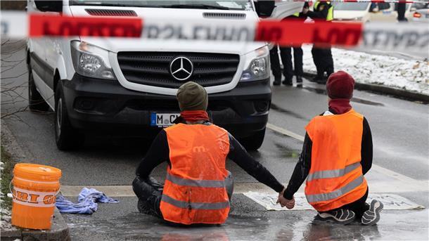 Zwei Klimaaktivisten der „Letzten Generation“ versuchen, sich auf einer Straße in München trotz Nieselregen und Minusgraden festzukleben.