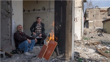 Zwei Männer wärmen sich in den Trümmern eines zerstörten Hauses in Kahramanmaras an einem Feuer. Im Zentrum der Stadt waren bei dem Beben vor einem Jahr unzählige Häuser zerstört oder beschädigt worden.