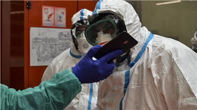 Zwei Mitarbeiter in Schutzanzügen schauen in einem Krankenhaus auf das Smartphone eines weiteren Angestellten.