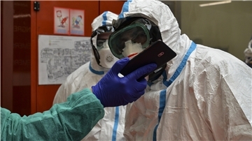 Zwei Mitarbeiter in Schutzanzügen schauen in einem Krankenhaus auf das Smartphone eines weiteren Angestellten.