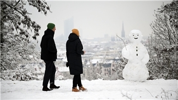 Zwei Spaziergänger wandern am Fockeberg (Leipzig) an einem Schneemann vorbei.