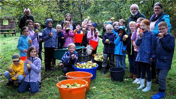 Kinder knien und stehen um Eimer herum, die mit Äpfeln gefüllt sind. 